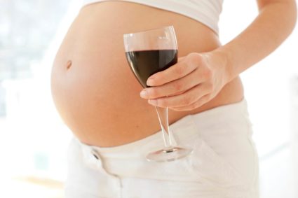 Беременная держит в руке бокал с вином 